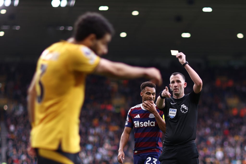 Referee Chris Kavanagh shows Rayan Ait-Nouri of Wolverhampton Wanderers (obscured) a yellow card